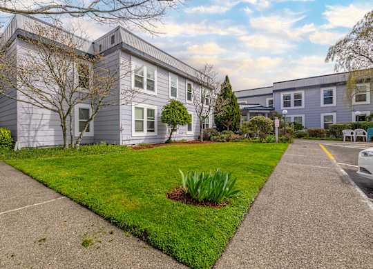 A grey house with a green lawn and a white car parked in front.