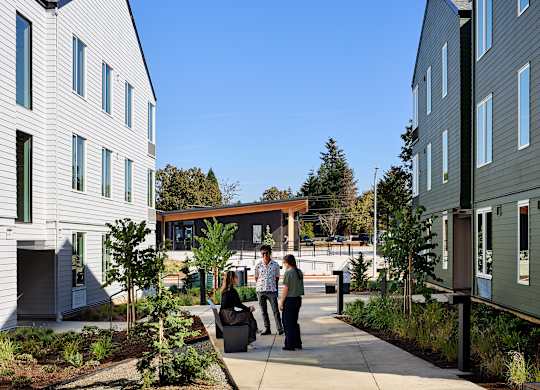 A group of people are walking down a sidewalk between two buildings.