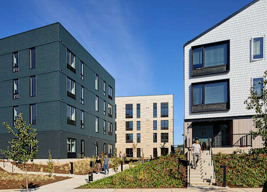A modern building with a green and white exterior is surrounded by a grassy area and a clear blue sky.