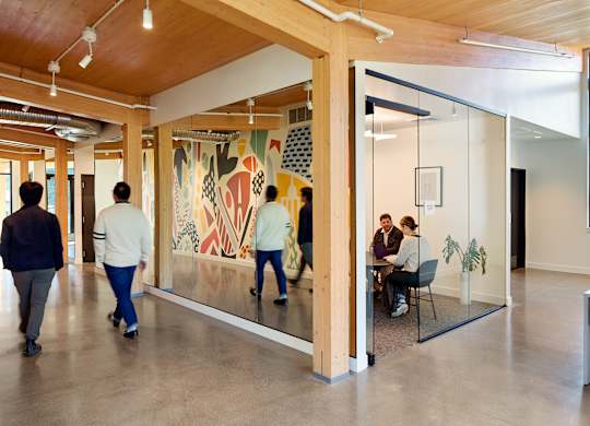 People walking in a hallway with a large painting on the wall.