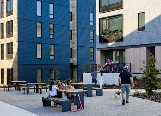 A group of people are sitting at a picnic table outside of a building.