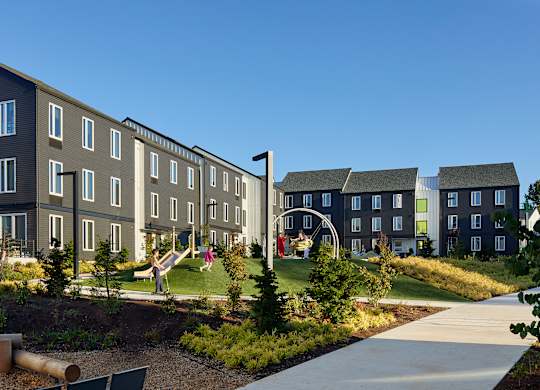 A playground area in front of a building with a slide and a swing set.