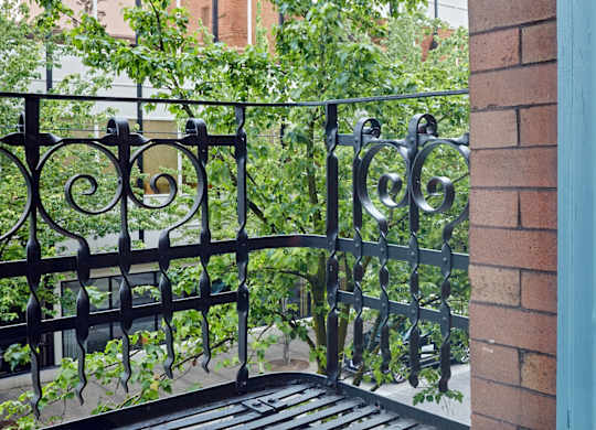 A black wrought iron gate with a brick wall on one side and a metal railing on the other.