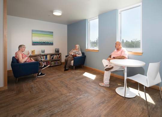 Three people sitting in a room with a white table and chairs.
