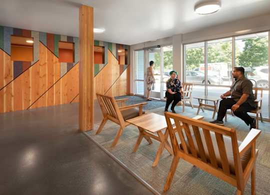 A group of people are sitting in a room with wooden chairs and a wooden wall.