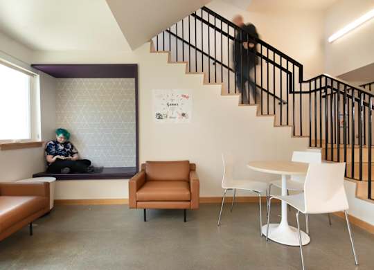 A person is sitting on a bench in a room with a staircase.