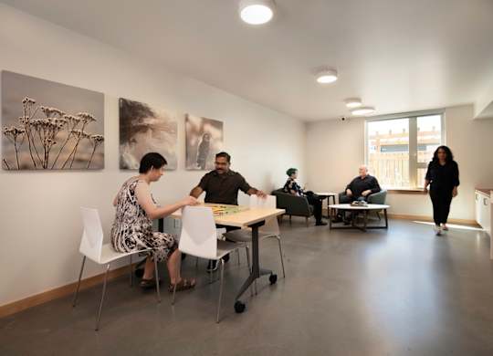 A group of people are sitting around a table in a room with artwork on the wall.
