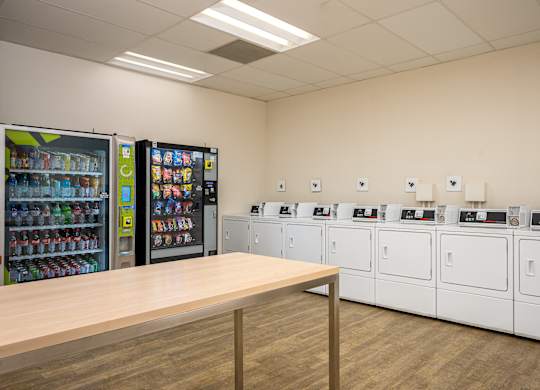 A room with a row of washing machines and a wooden table in front of them.