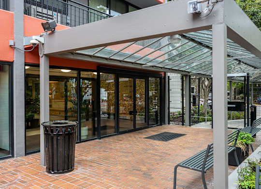 A glass door entrance to a building with a trash can and benches outside.