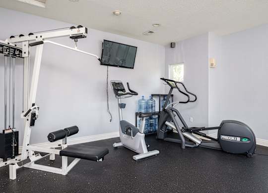 A home gym with a variety of equipment including a weight bench, a treadmill, and a television.