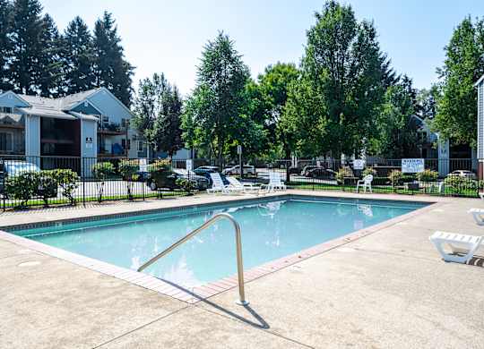 A swimming pool surrounded by trees and a building in the background.