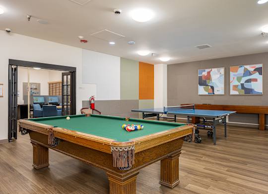 A pool table in a room with a ping pong table and two paintings on the wall.