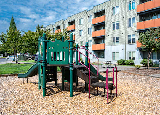 A playground with a green slide and a red swing set.