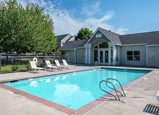 A pool with a diving board and lounge chairs in front of a building.