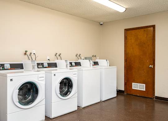 A row of white front load washing machines are lined up in a laundromat.