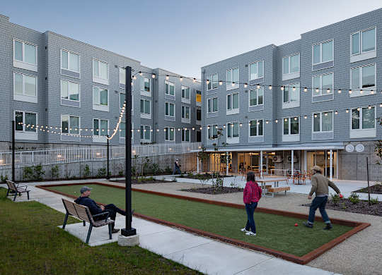 A man is sitting on a bench in a courtyard with a woman and a child playing.
