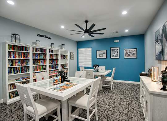 A room with a white table and chairs, a bookshelf, and a ceiling fan.