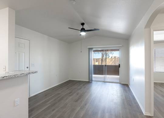 A spacious room with a ceiling fan and sliding glass doors leading to a balcony.