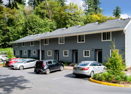 a parking lot in front of a gray building with cars parked