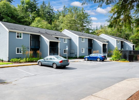 a parking lot in front of two apartment buildings with cars parked in front