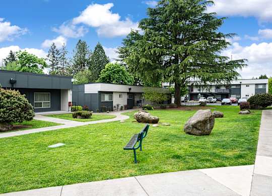 A park with a bench and a few rocks in the foreground and a building in the background.