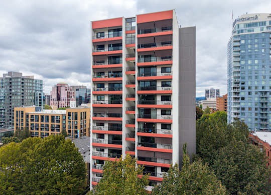 A tall red and grey building stands in front of a row of trees.