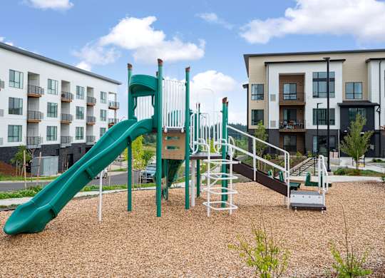 A playground with a green slide and a brown sandy area.