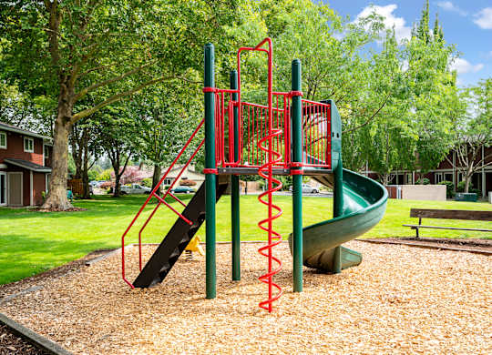 A playground with a red and green slide and a brown bench.