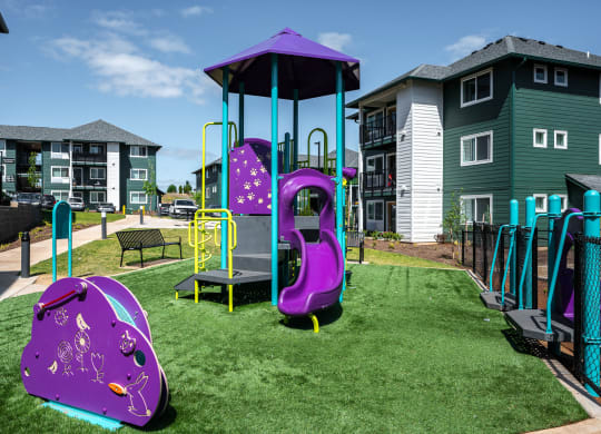 a playground with a purple swing set and play equipment in front of apartments