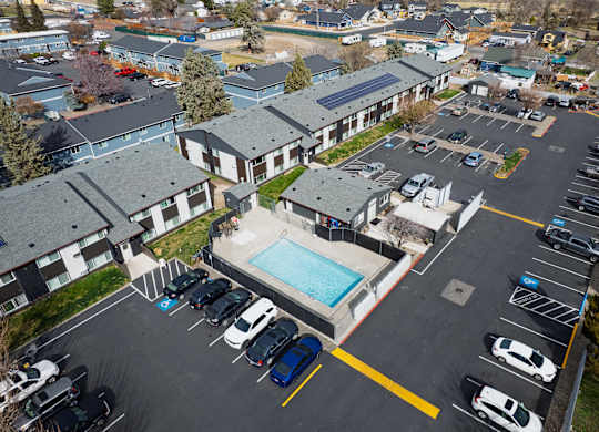 A parking lot with cars and a swimming pool in front of apartment buildings.
