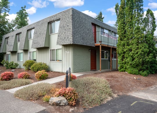 the front of a green apartment building with a sidewalk and landscaping