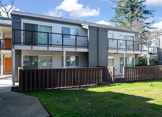 A modern two-story apartment building with a balcony and a fence.
