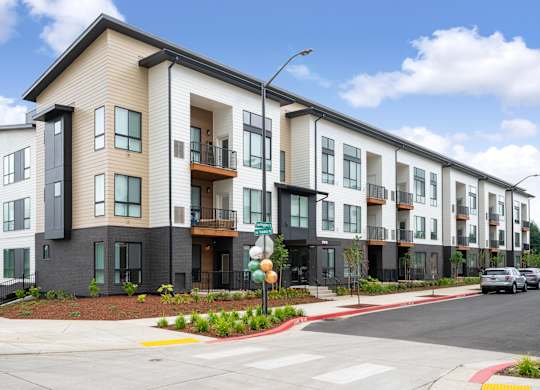 A street view of a modern apartment building with cars parked on the street.