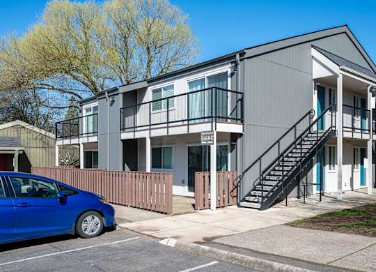 A blue car is parked in front of a grey apartment building.