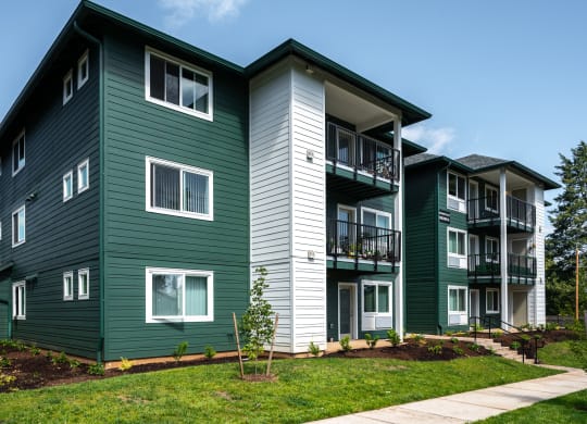 a green apartment building with a sidewalk in front of it