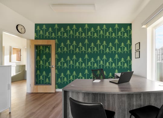 a home office with a desk and a green wall with trees on it