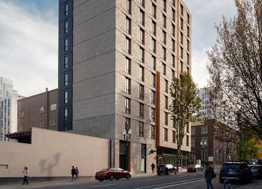 A tall building with a grey facade stands on a street corner with cars and pedestrians.