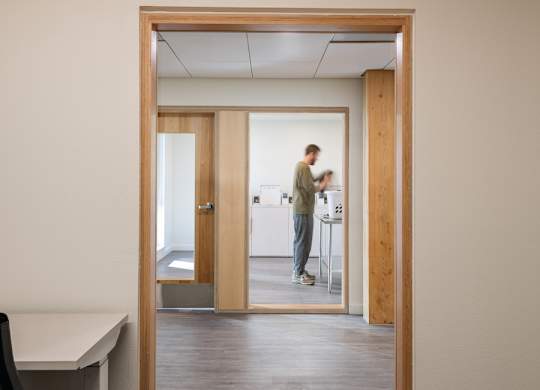 A man is standing in a room with a white desk and a mirror.