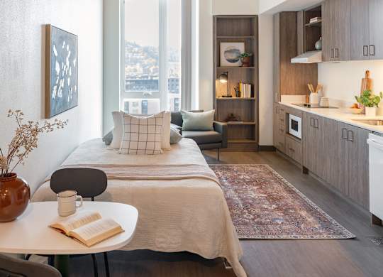 A modern bedroom with a bed, a table, a chair, a vase, a book, and a cup on the table.