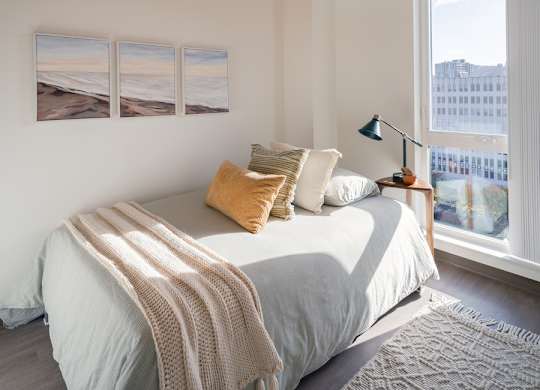A bedroom with a bed, pillows, a blanket, a lamp, and pictures on the wall.