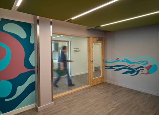 A person walks through a doorway into a room with a blue and pink wall mural.