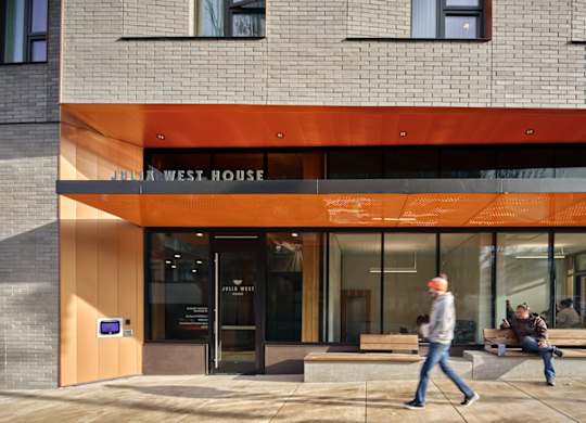 A man is walking past a building with a sign that reads "Jim West House.".