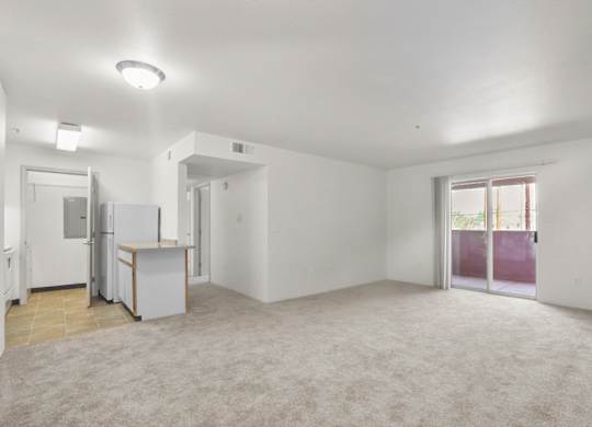 A spacious, empty room with a kitchenette and sliding glass doors.