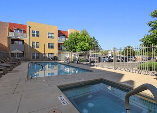 A pool area with a hot tub and lounge chairs in front of apartment buildings.