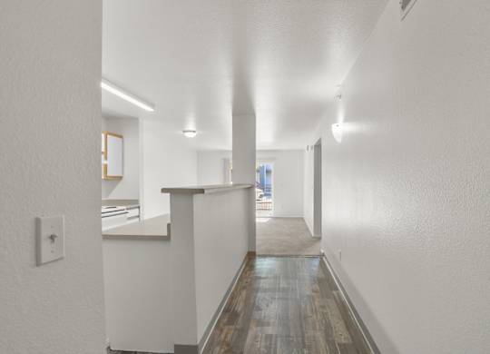 A long hallway with a white wall and a wooden floor.