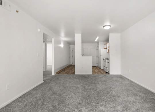 A spacious, empty room with white walls and a grey carpet.