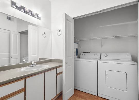 A white bathroom with a sink, mirror, and washer and dryer.