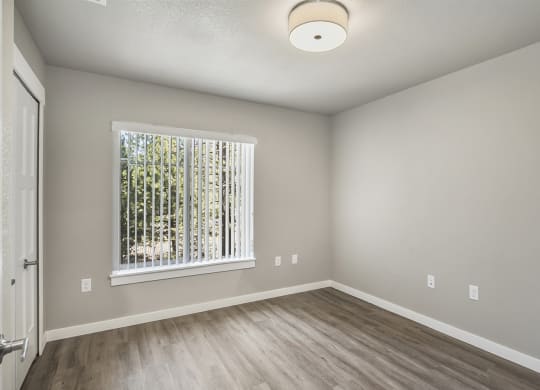 an empty bedroom with a large window and hardwood floors