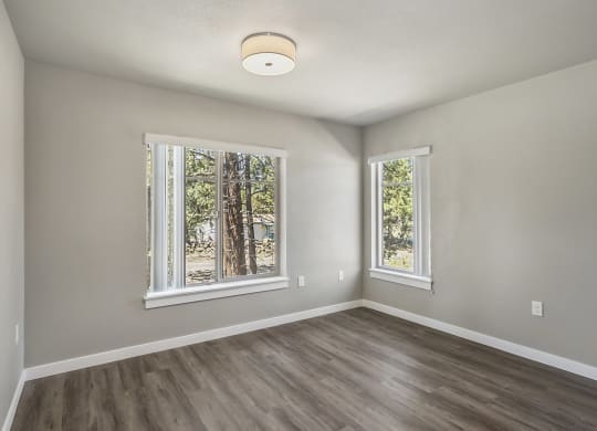an empty bedroom with a large window and hardwood floors