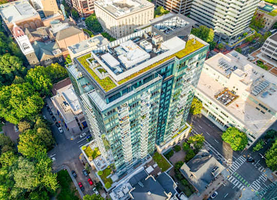 A modern building with a green roof is surrounded by other buildings and trees.